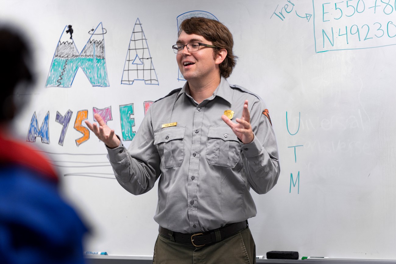 Chris Silcox, Education Ranger, talks to school group in front of a white board in the Schoodic education classrooms. Ranger talks to school group in front of a white board.