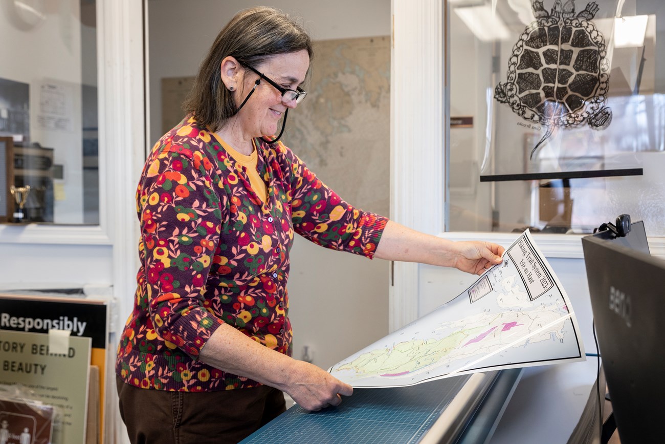 Karen holding and examining a recently printed map that she made in a park office. Woman holding and examining a recently printed map.