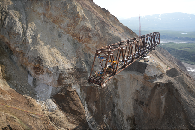 A bridge truss rests on rocky cliff in preparation for installation.