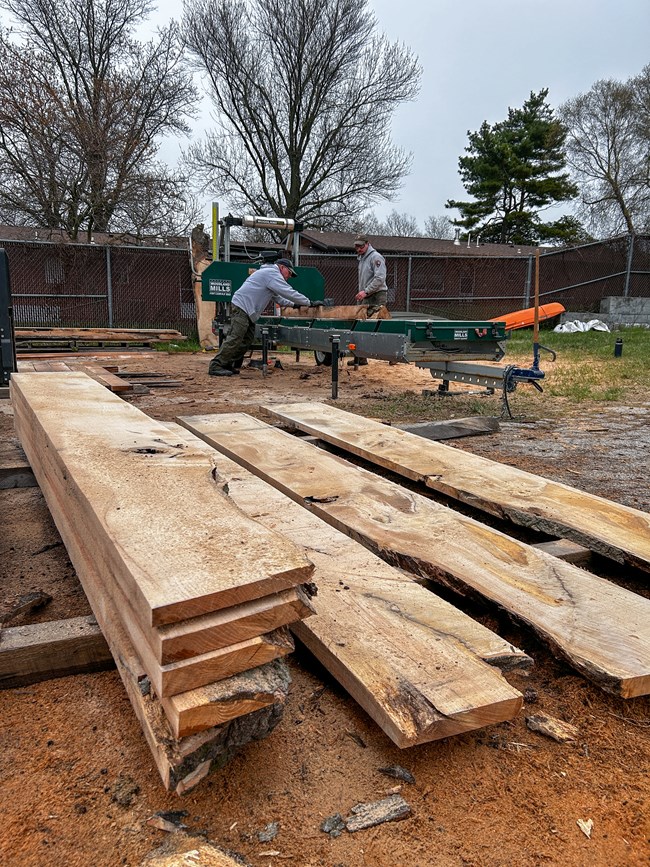 Lumber milled at Fort McHenry NMHS with milling equipment in the background.