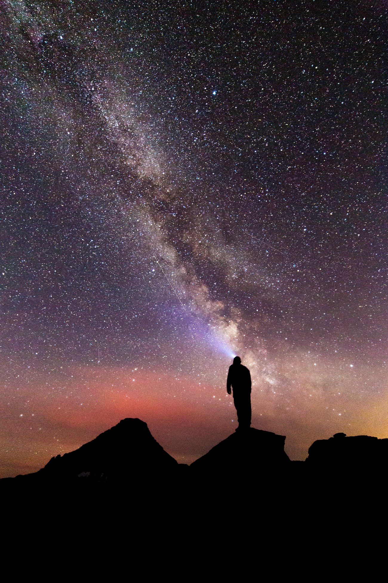 A hiker with a headlamp looks up towards the night sky