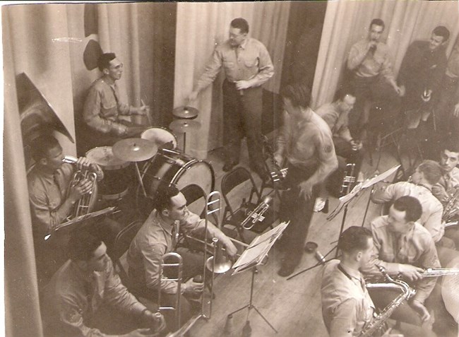 Group of soldiers sitting and standing, playing drums and brass instruments.