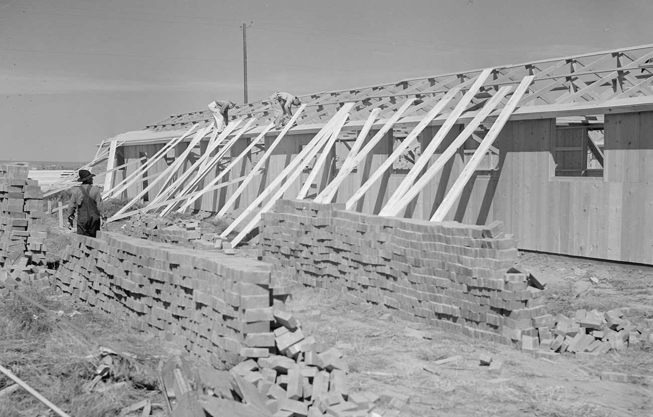Contractors assembling buildings Men stand on and near a building under construction with large piles of bricks nearby