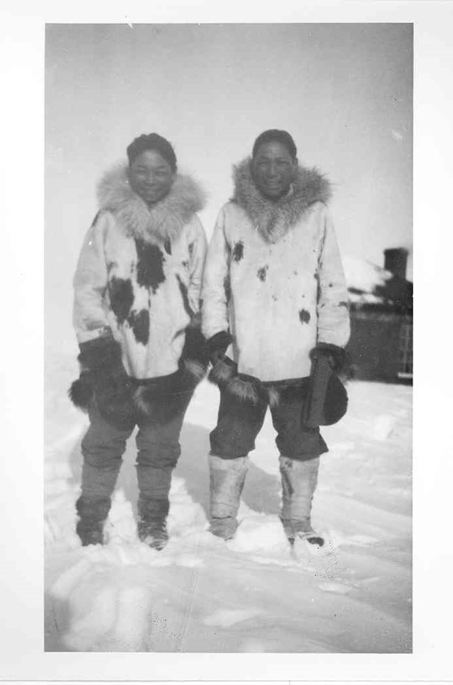 Two young men wearing mukluks and white spotted reindeer parkas.