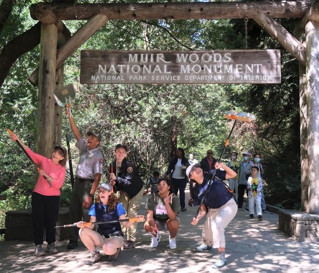 22 GOGA NPLD-1 A group photo of volunteers and a park ranger posing a silly photo under the park entrance sign after a National Public Lands Day event at Muir Woods National Monument.