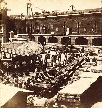 Men inside Fort Sumter gathered around long table. Crane and cannons on parapet of fort behind them.