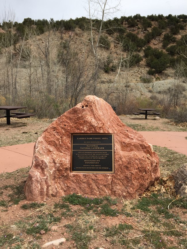 Boulder with plaque in foreground with sparsely vegetated hillside in background