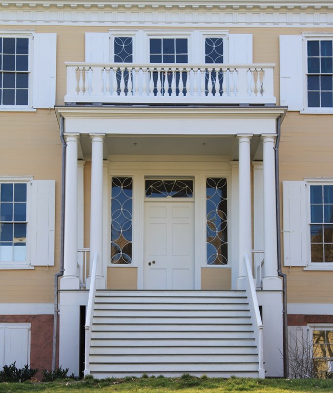 The entrance of the Grange, with a staircase leading up to a white door and ornate windows in either side of the door.