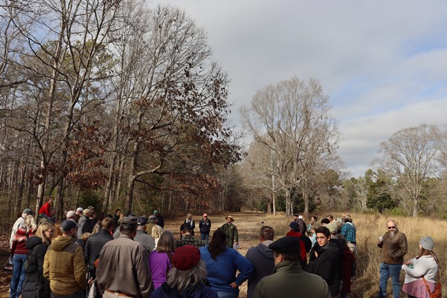 Park ranger stands in a crowd of people outdoors and speaks to visitors