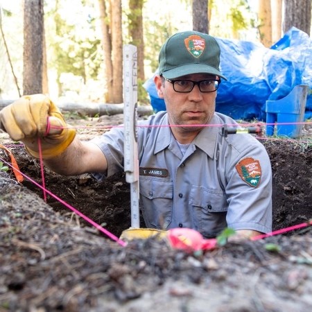 a park ranger in a pit in the ground and measuring a string to begin an archeological survey