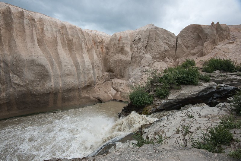 photo of a stream flowing past a steep bank of fine-grained rock