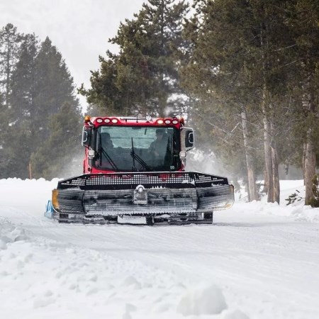 a large groomer machine driving down a snow-covered road