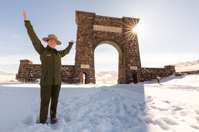 a park ranger in uniform standing in snow beneath a large stone archway
