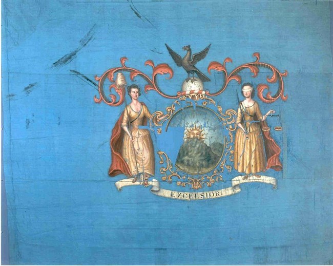 A blue rectangular flag. A coat of arms sits in the center. It has Ladies Liberty and Justice framing it with a sailing ship in the center.