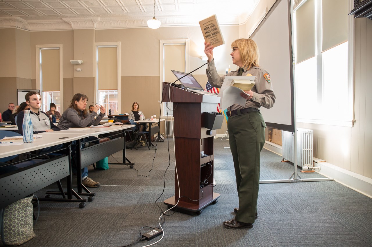 A park ranger speaking at a podium holds up a book.