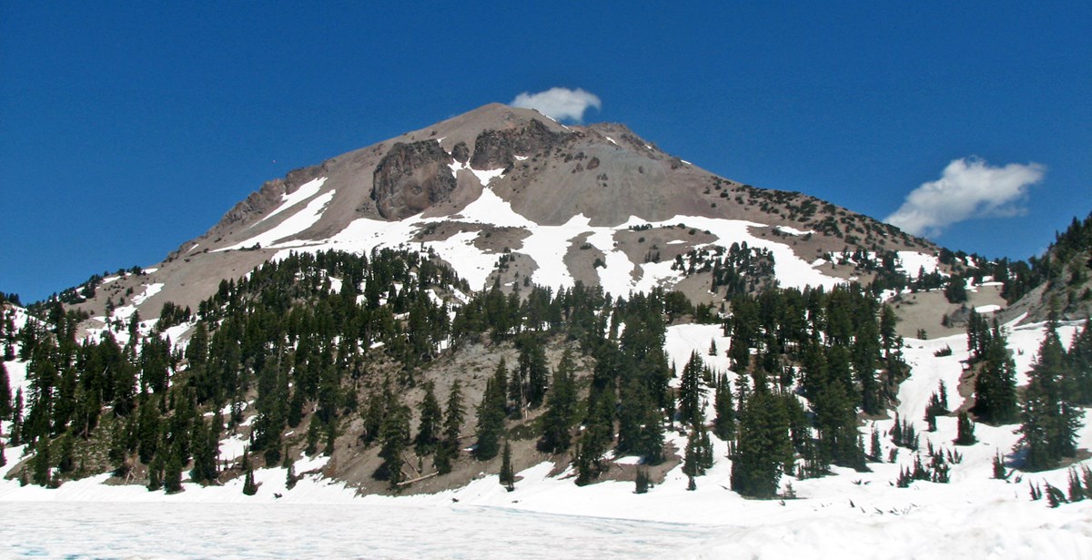 photo of a volcanic peak with snow cover and trees on its lower slopes