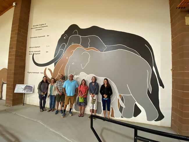 Group of people standing in front a mastadon wall art