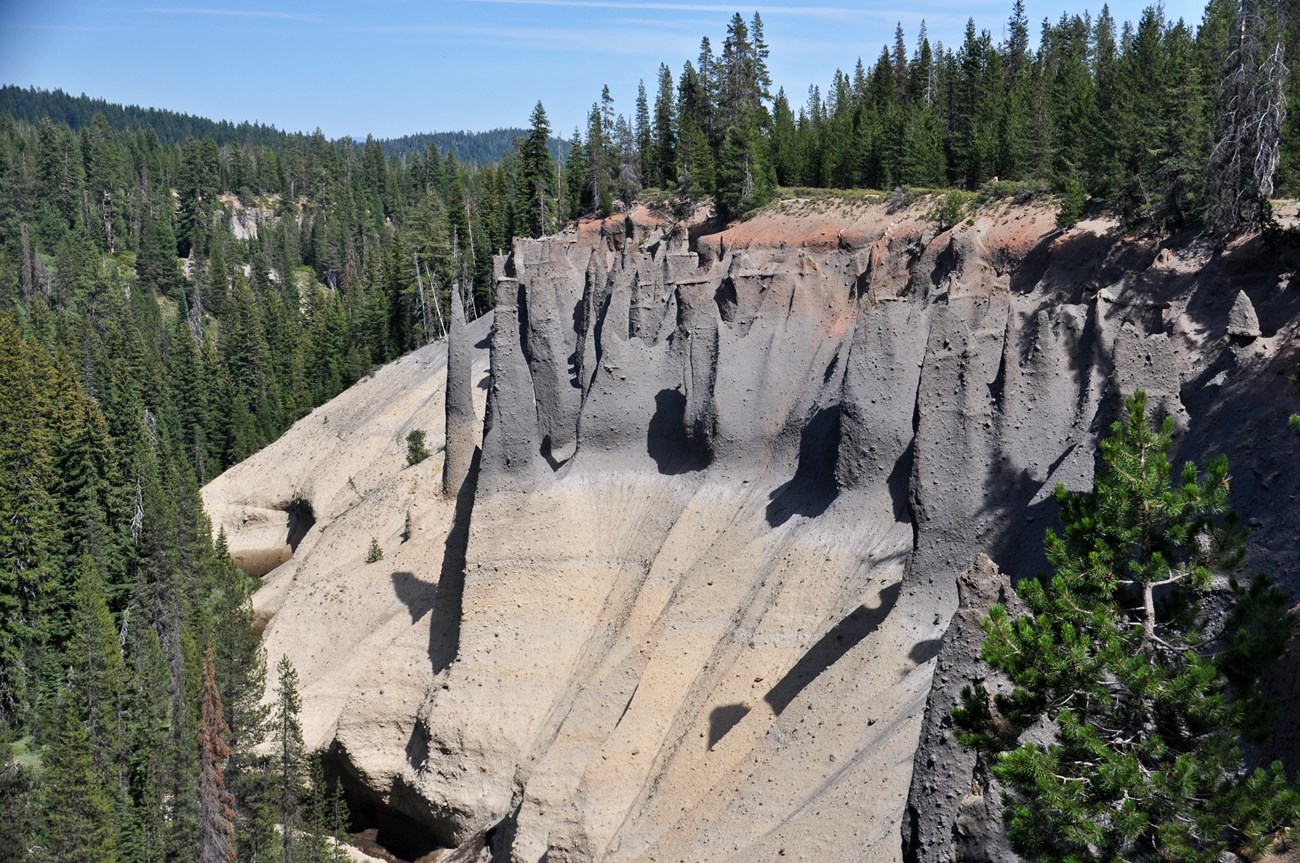 Photo of layered rock outcrop with unusual erosional features surrounded by forested hills