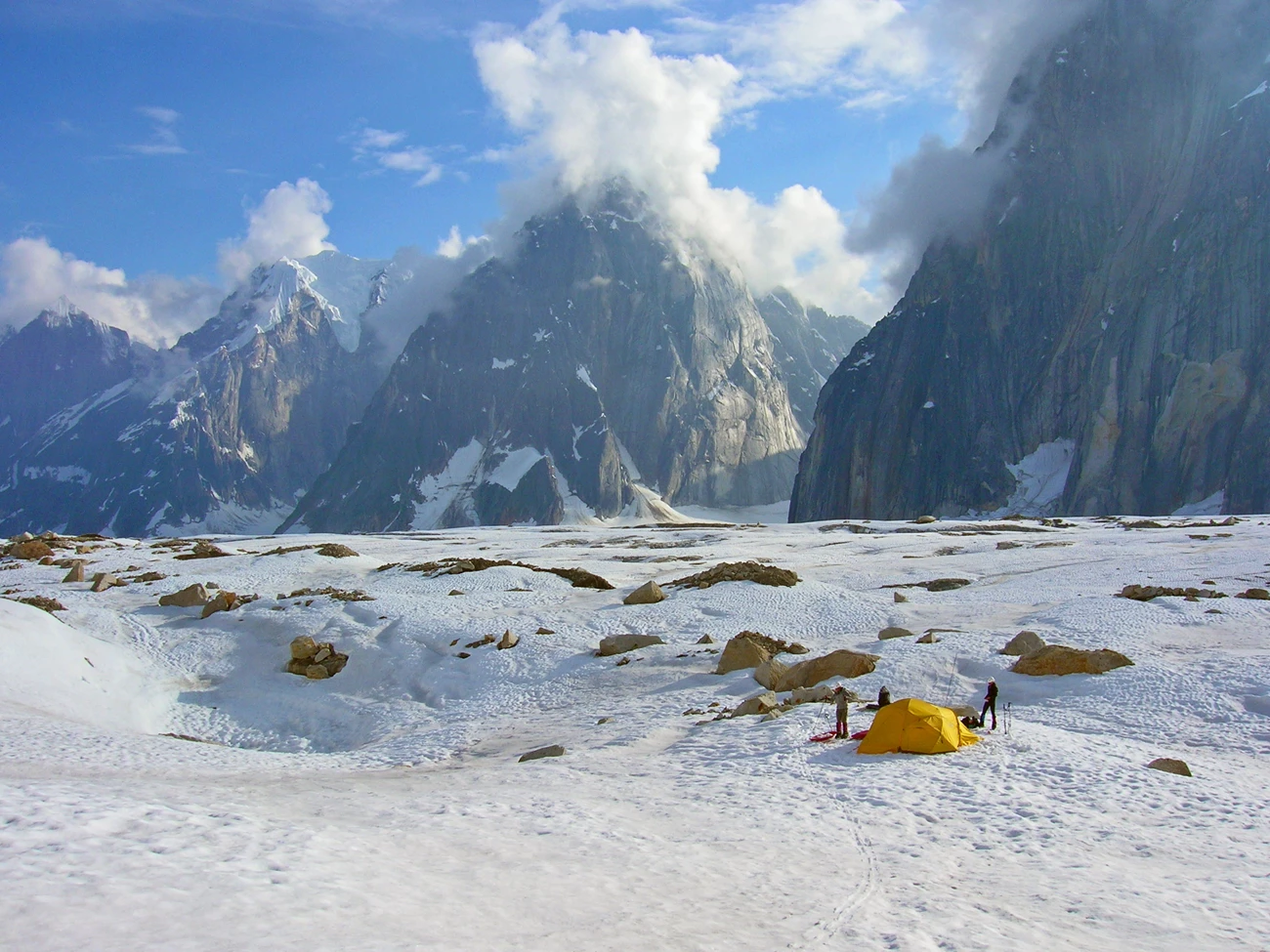 Camping in Ruth Gorge Tents dot a snowy field, sheer-sided mountains rising in the distance.