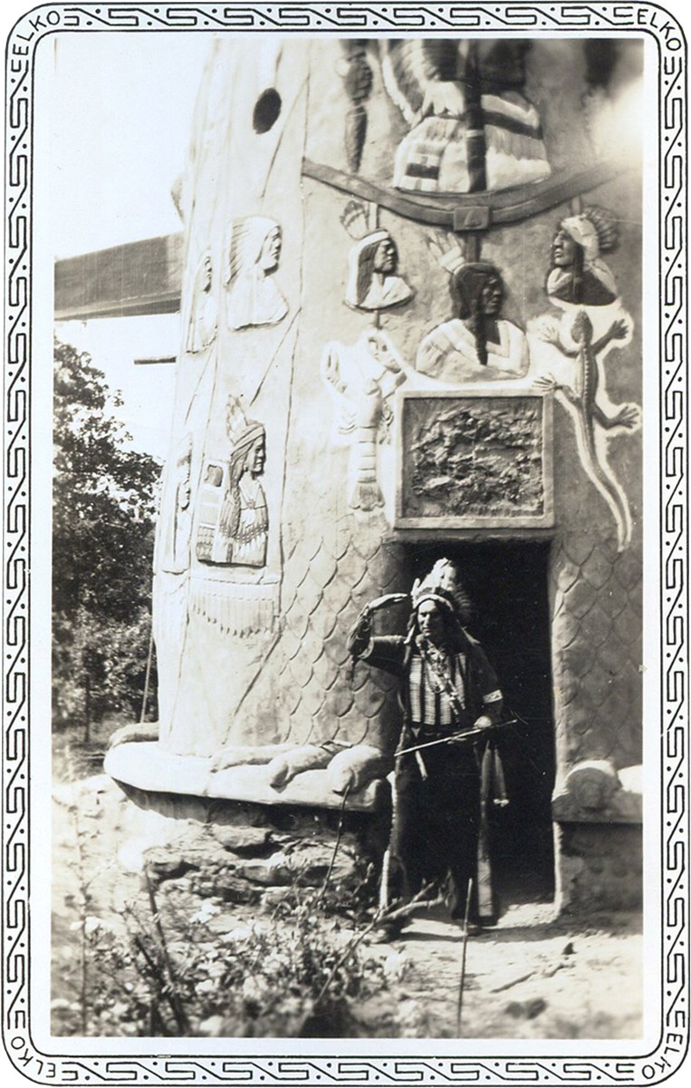 Totem Entrance Man in Indian feather headdress and costume standing in doorway to totems with images of native Americans.