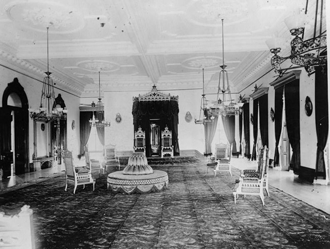 Two fancy chairs sit on a raised platform at the center of the back wall of a room