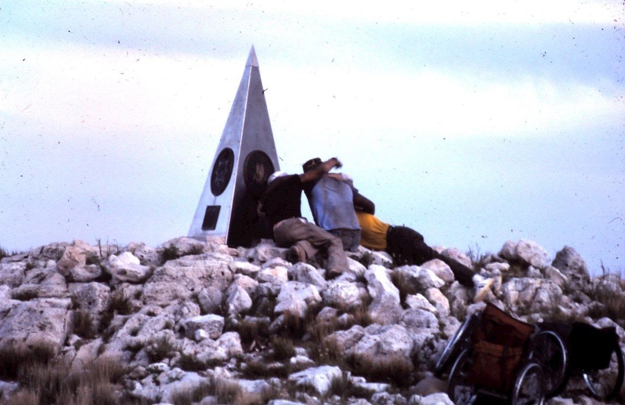 Three men touch a summit monument