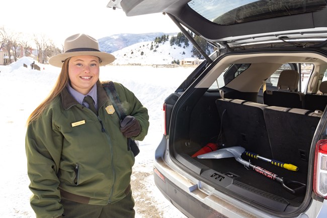 A park ranger prepares their vehicle for a winter drive with a snow shovel and backpack filled with supplies.
