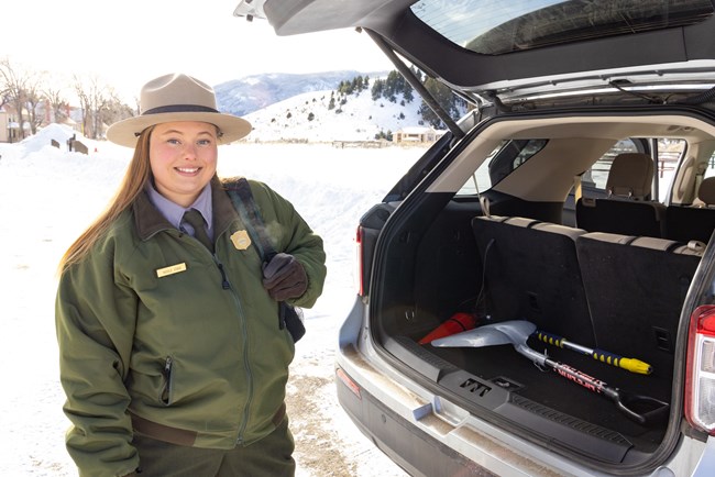 Watch Out for Winter Conditions A park ranger prepares their vehicle for a winter drive with a snow shovel and backpack filled with supplies.