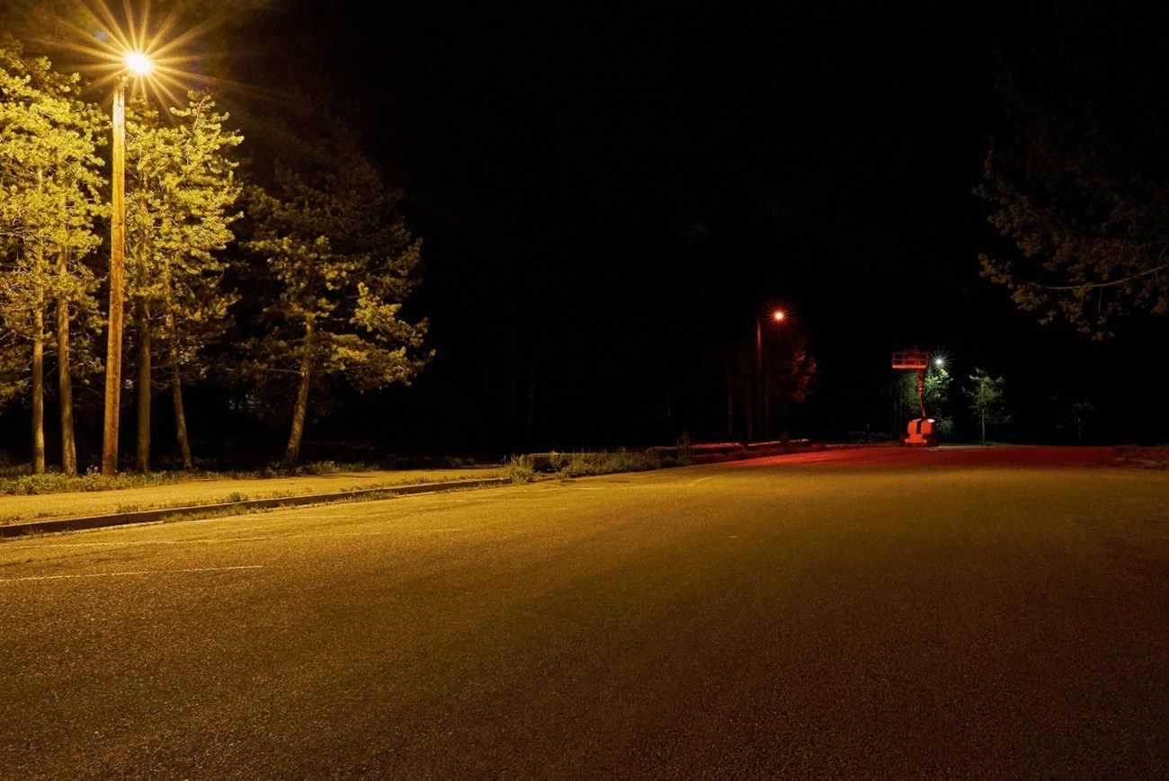 Different colored streetlights Looking down an empty parking lot at night lined with streetlights of different colors. There's a bright, yellowish standard light in the front left, then a red light, and then a cool white light in the distance.