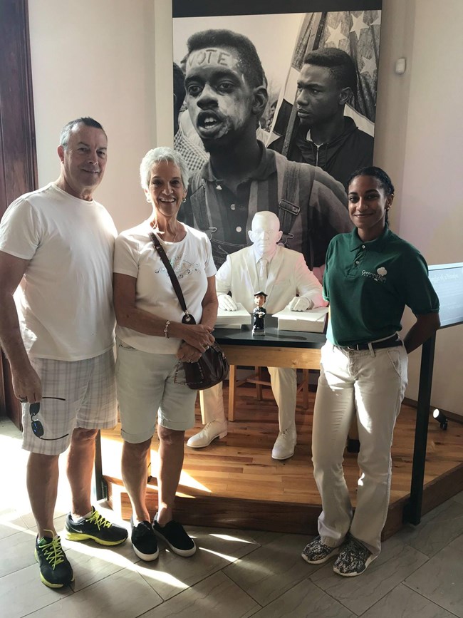 a park rangers poses with two visitors inside a museum