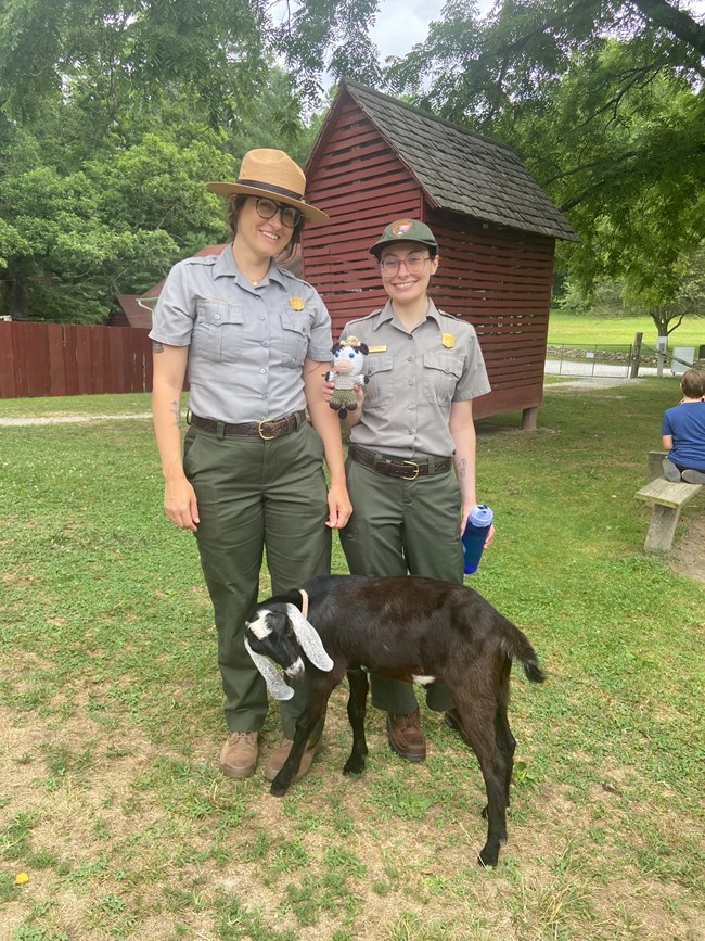 Ranger Cow and two rangers take a photo next to a goat Two park rangers take a picture with ranger cow and a goat