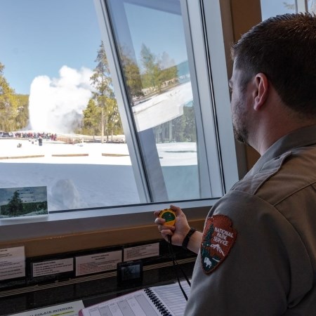 a park ranger holding a stopwatch and watching a geyser erupt