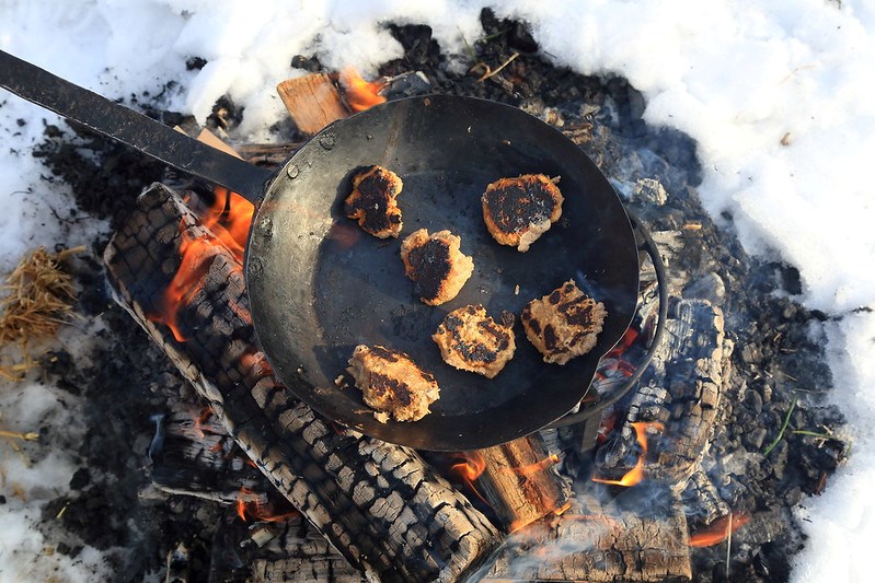 globs of a dough-like substance cook in an iron skillet over a campfire