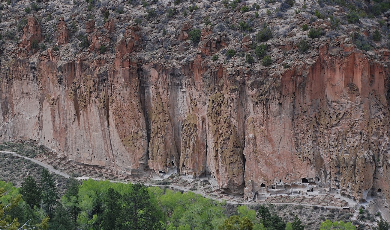 Photo of a tall cliff with windows and doors carved in to the rock at the base.