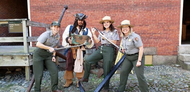 3 park rangers standing with a man in a pirate costume
