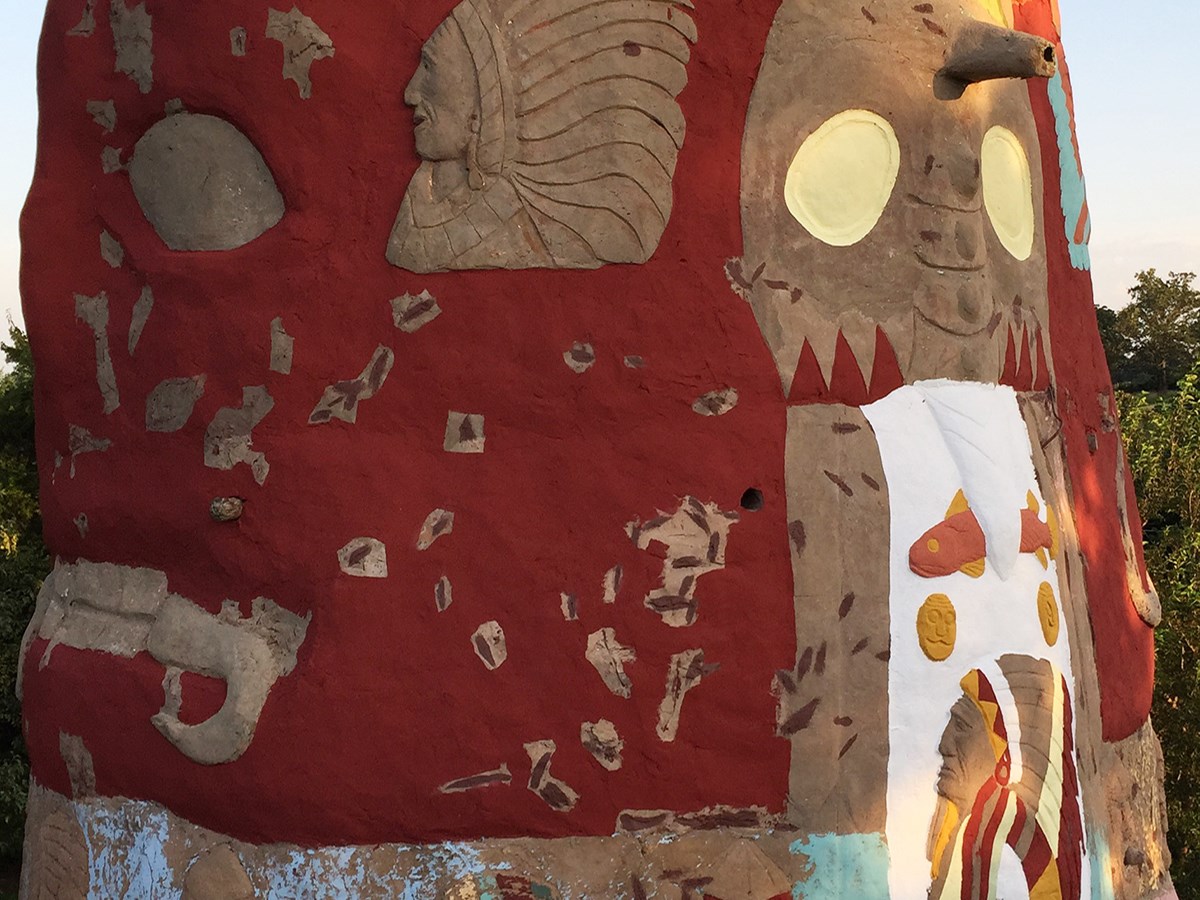 Totem Close-up Close up flaking red rectangular shape with exposed rust and carved busts of Indians in feather headdresses.