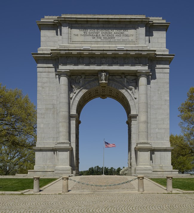 Memorial Arch at Valley Forge NHP Stone Arch at Valley Forge National Historical Park with American Flag on flagpole visible in distance through the arch
