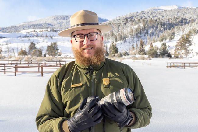 A park ranger holds a camera with a telephoto lens for wildlife photography.