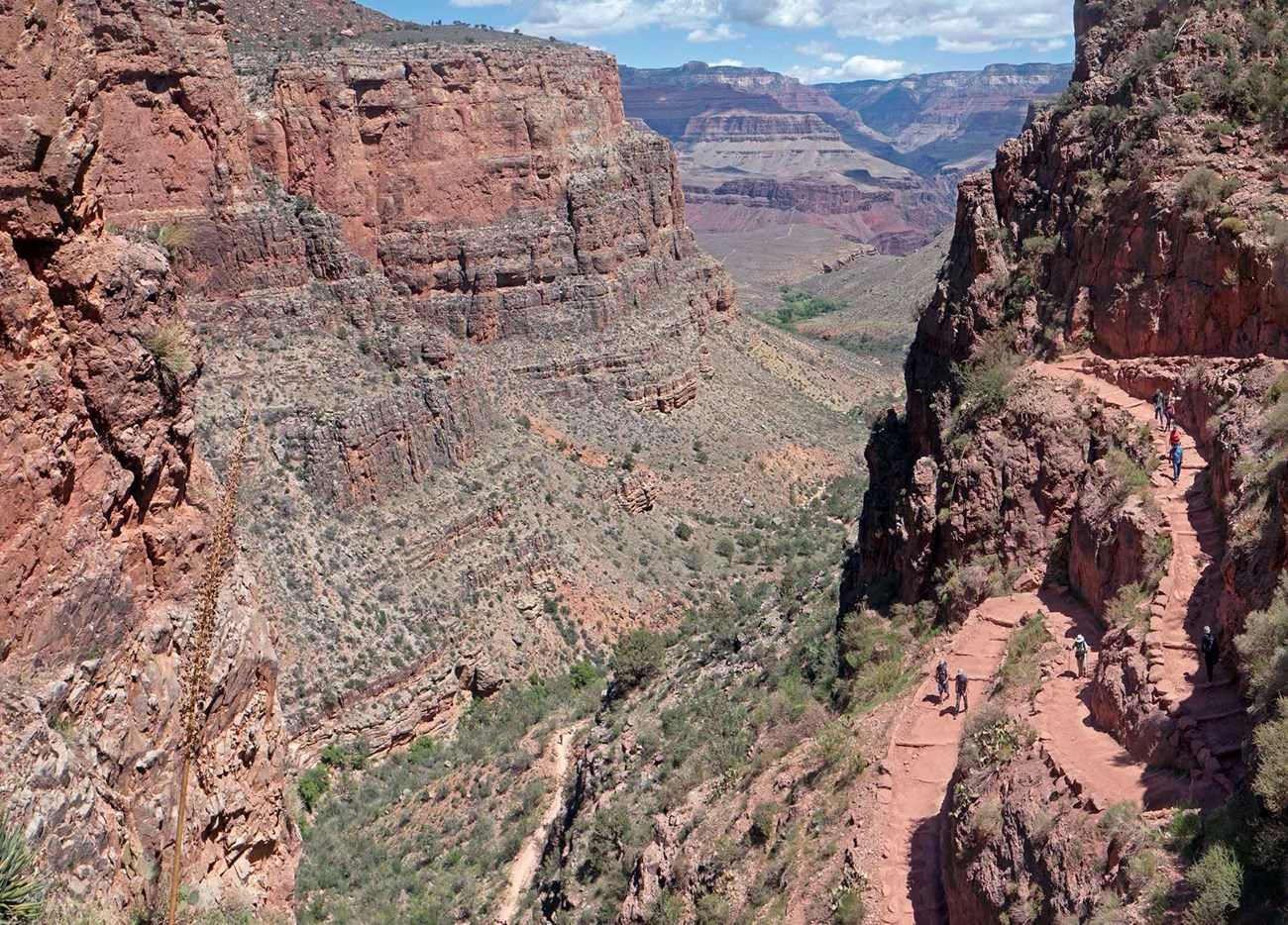 several groups of hikers descending steep switchbacks within a sheer cliff that is hundreds of feet above the valley below.