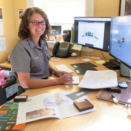 a woman sitting at a desk with design plans spread out on the desk