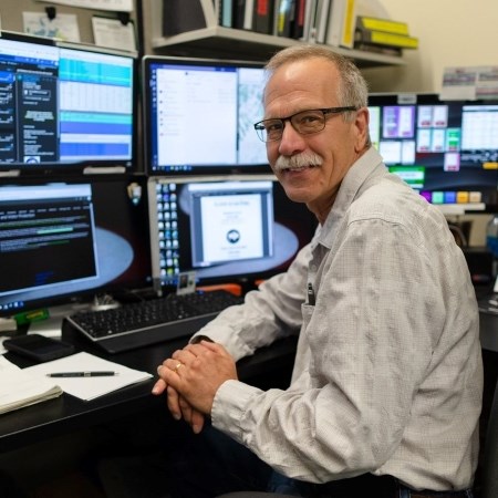 a man sitting at a desk with a bunch of computer monitors