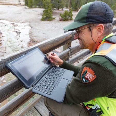 a park ranger with a computer next to a hydrothermal feature on a boardwalk