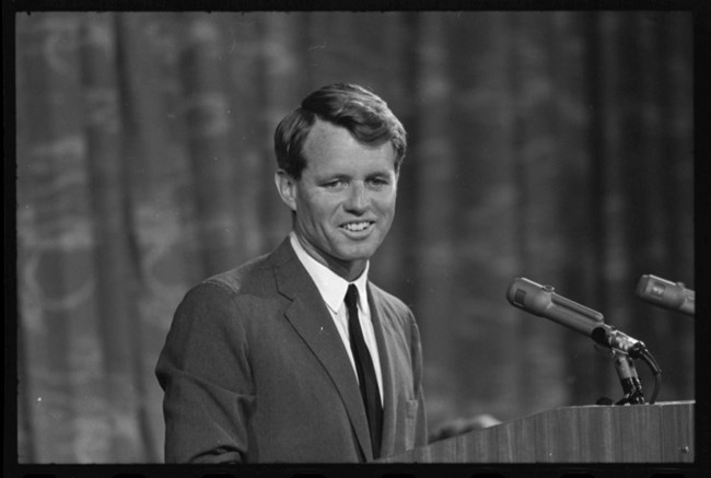 A black and white photo of Robert F. Kennedy at a podium.