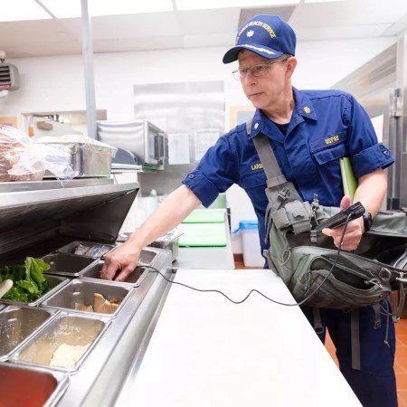 a man in uniform testing temperatures of food in an assembly line