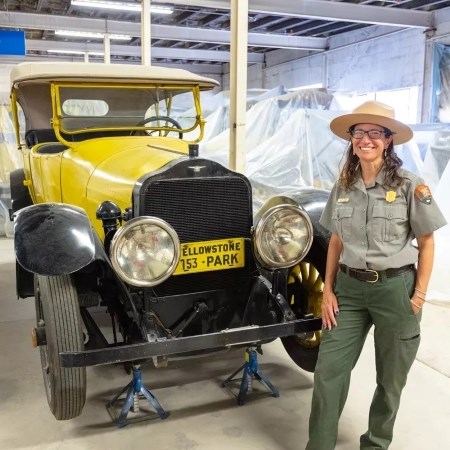 a park ranger standing next to a historic vehicle