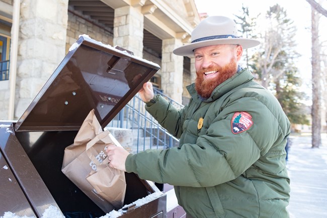 a park ranger throwing trash away in a trashcan