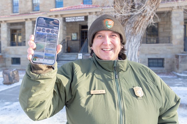 Expect Limited Services a park ranger holding up a phone with the Yellowstone app on the screen