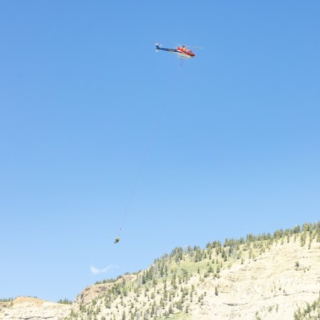 a person dangling on the end of a rope suspended underneath a hovering helicopter