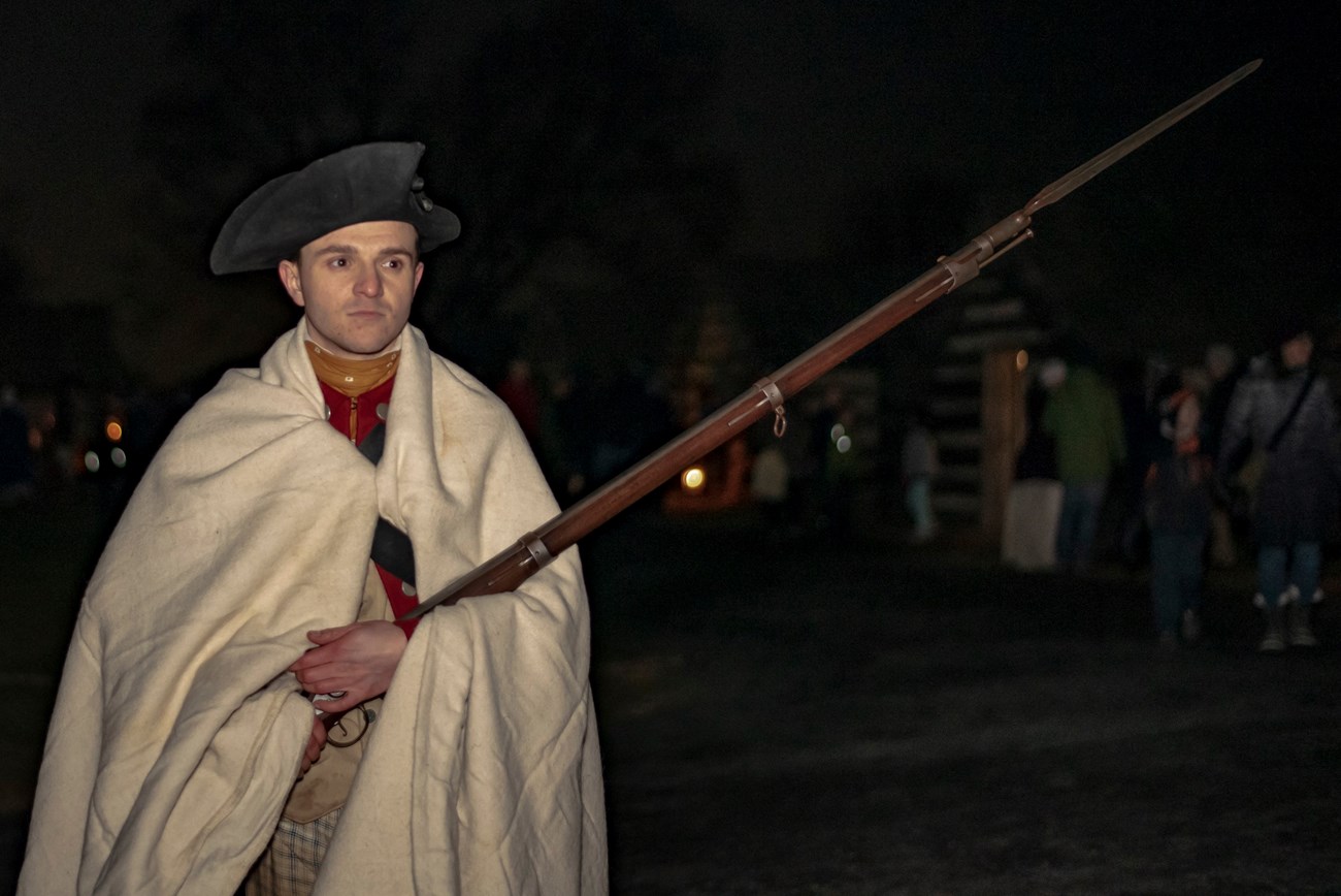 a man with a blanket draped over his shoulders holding a musket