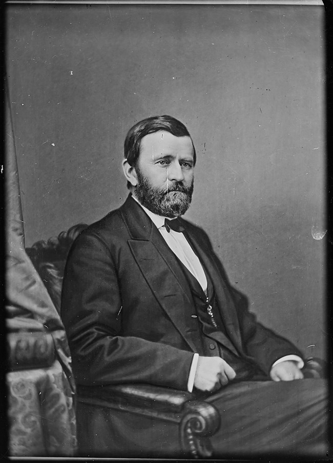 man with a beard and suit sitting in a chair and posing for a photo.